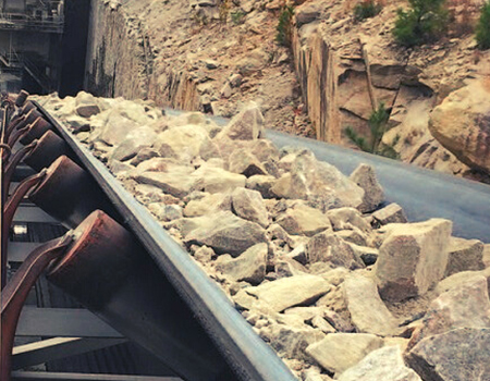 Conveyor belt hauling large brown rocks.