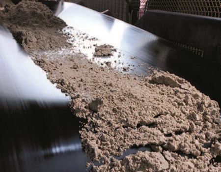 Brown powder being transported on conveyor belt.