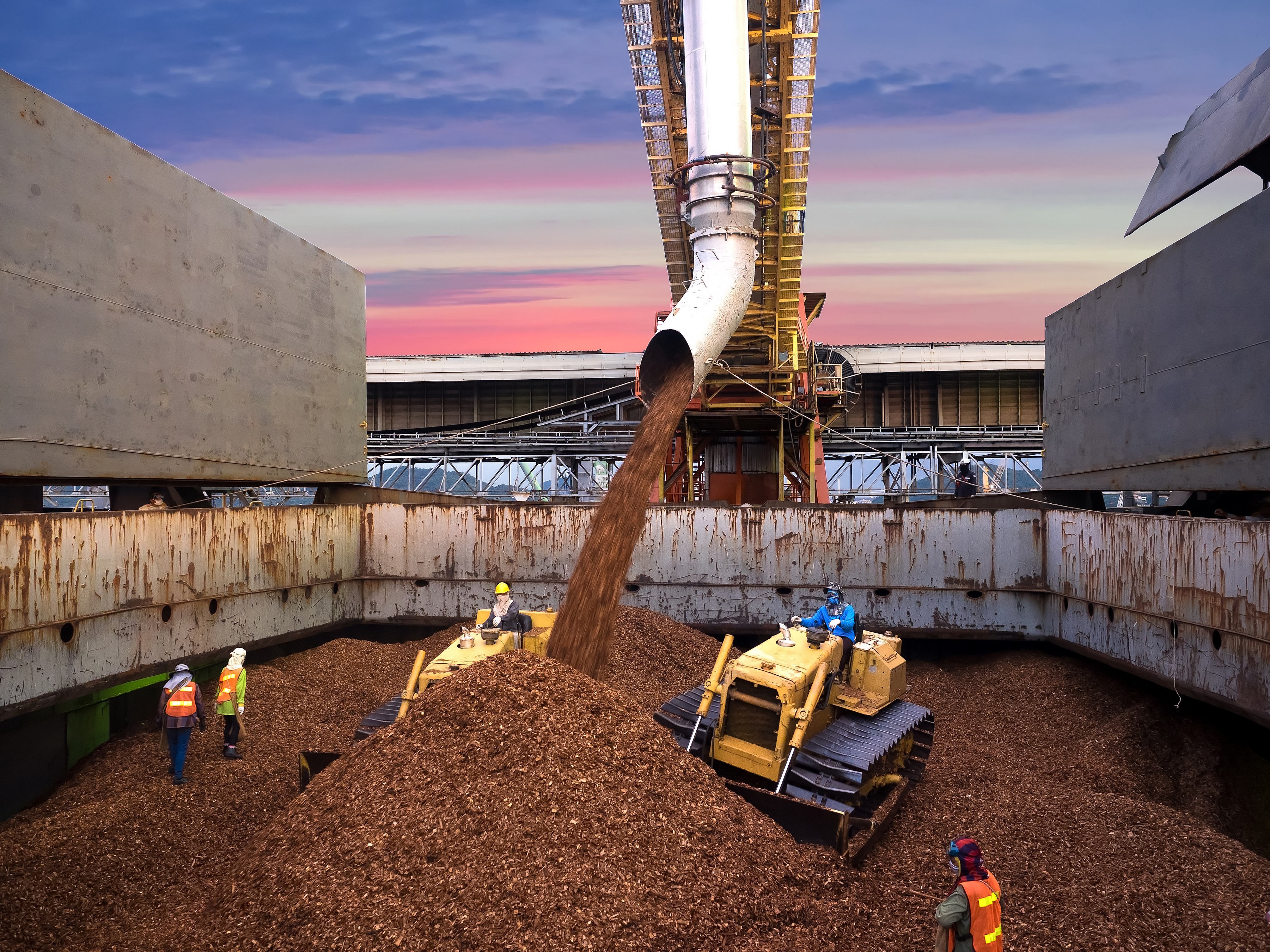 Large heap of material being distributed with heavy equipment.