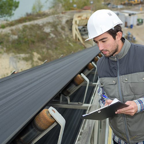 Technician wearing a hardhat inspecting a conveyor belt